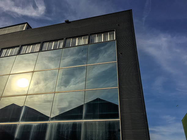 Low angle close-up view of a modern commercial building exterior featuring a combination of reflective glass curtain walls and corrugated metal cladding.