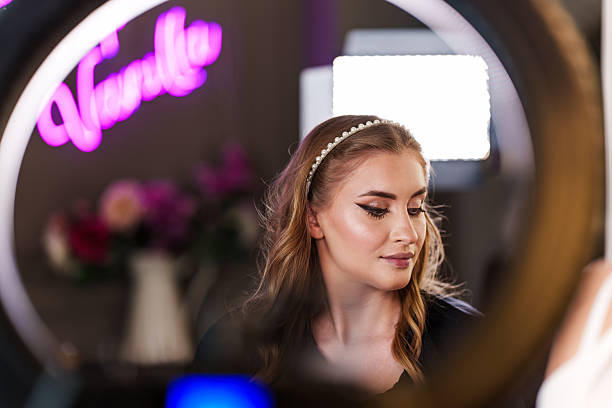 Young women showcasing glamour make-up, wearing a pearl headband and framed by a ring light in a vibrant studio shot with neon lighting.