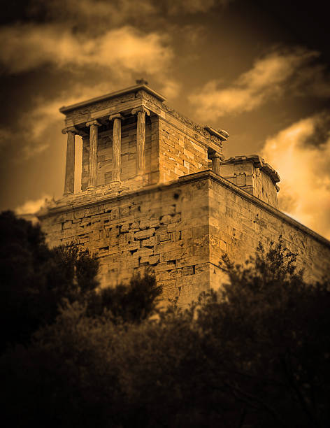 black and white sepia toned view from below of the Temple of Athena Nike, located in a corner of the Acropolis, and perched on a massive stone bastion made of weathered stone blocks, Athens