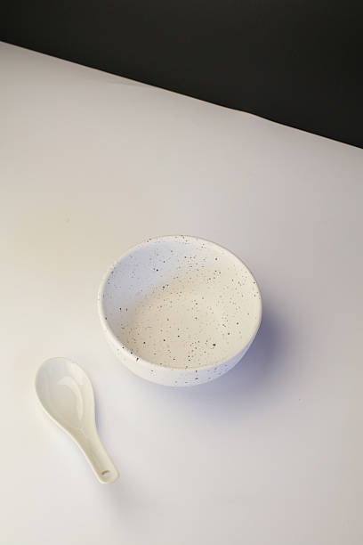 Empty white ceramic bowl with spoon on table with black background. Kitchenware elegant design