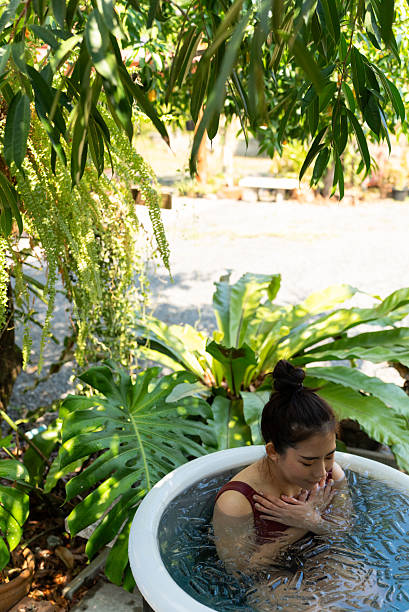 Vertical high angle view of woman practicing outdoor ice bath cold water therapy surrounded by green nature plants, health wellness and longevity lifestyle for immune support and inflammation relief.
