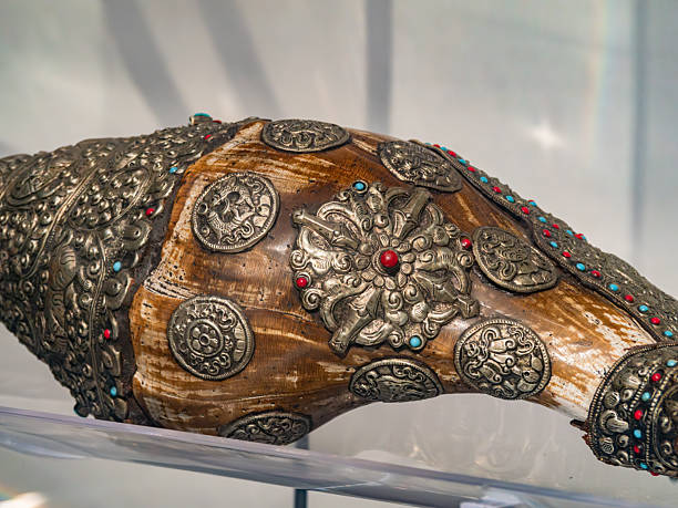 This image showcases a sacred Tibetan Buddhist ritual object known as a Dungkar, or white conch shell. The natural white shell is encased in elaborate, high-quality silver metalwork featuring intricate filigree and repoussé techniques. The silver mounting is heavily embellished with turquoise and coral inlays, forming traditional Himalayan floral and geometric patterns. At the center of the silver wing, a prominent circular turquoise stone is surrounded by smaller red coral beads, creating a vibrant focal point. The metalwork extends to a decorative tip and a wide, flared 