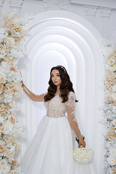 Bride in a wedding dress poses near floral decorations in a decorated venue during a ceremony