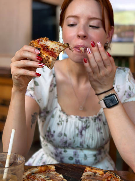 Close-up image of attractive, redheaded  woman eating thin, crispy crust Prosciutto Crudo pizza, melted golden buffalo mozzarella cheese, rich tomato sauce, displaying manicure nail art, restaurant setting, focus on foreground