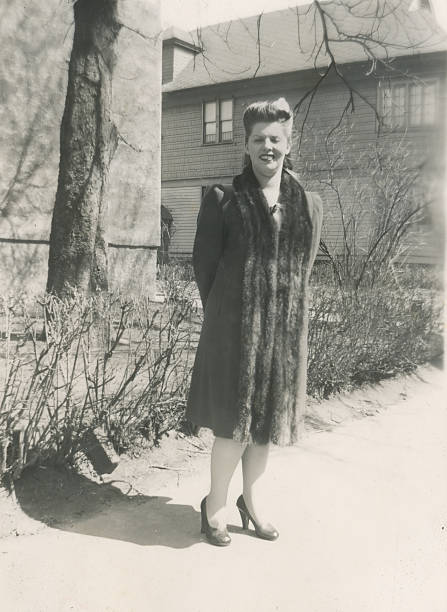 Black and white vintage portrait of a well dressed woman wearing a coat and fur stole standing outdoors in the mid 1930s.