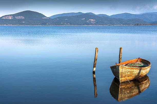 View of an old wooden boat moored on Lake Massaciuccoli in Torre del Lago. Calm blue water with reflections and hills in the background, Versilia, Lucca, Tuscany, Italy