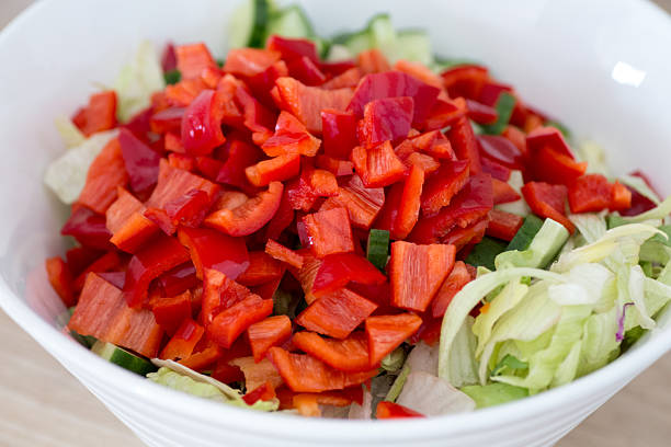 Chopped red bell peppers and fresh lettuce close-up in bowl