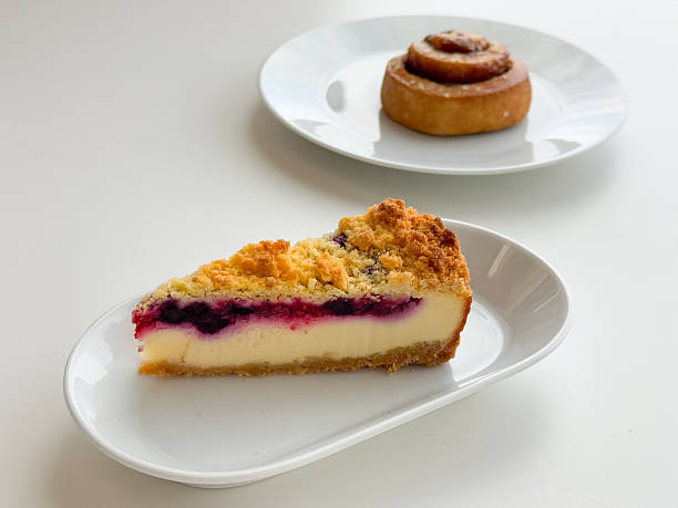 Blueberry cheesecake slice with cinnamon roll in soft focus on white tableware. Bakery assortment styling, dessert pairing, cafe selection, pastry presentation, minimal food composition concept