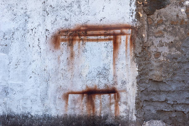 A close-up shot of a weathered concrete wall with visible rust stains forming an abstract square shape. The texture of the wall is aged and grunge, providing a unique and raw backdrop. The image features a combination of white painted areas and exposed concrete, creating a visually appealing contrast.