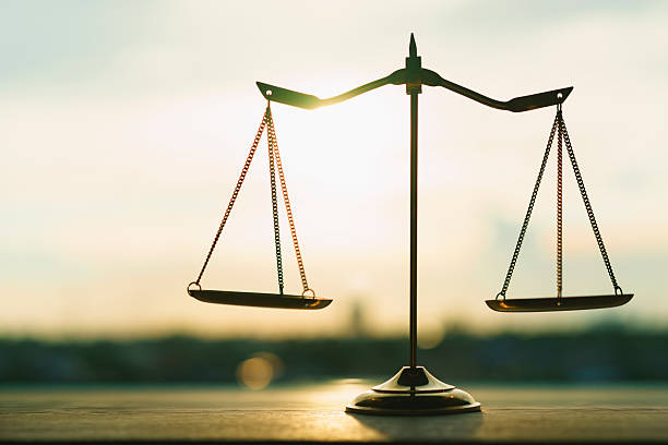 Silhouette of an empty classic balance scale against a bright sunset sky background. Symbolizes justice, equality, law, legal system, equilibrium, and ethical business choices.