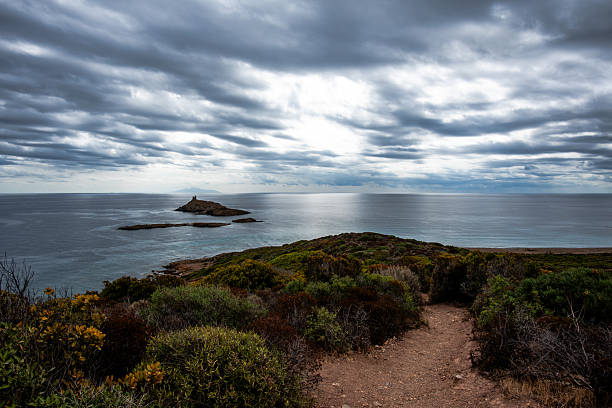 Rocky islet with a historic stone tower surrounded by calm sea under dramatic overcast sky. Ideal for travel, heritage and Mediterranean coastal themes.