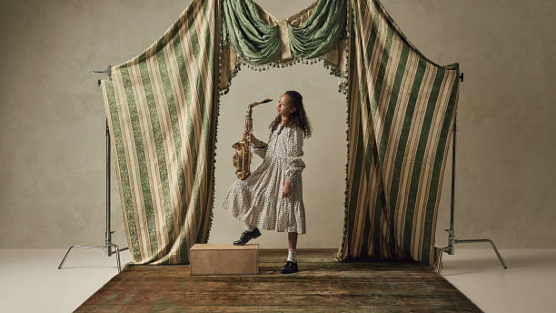 Young girl holding saxophone standing on platform in studio thoughtful portrait. Concept of decision making moment, future career choice, self reflection, identity search and personal direction.