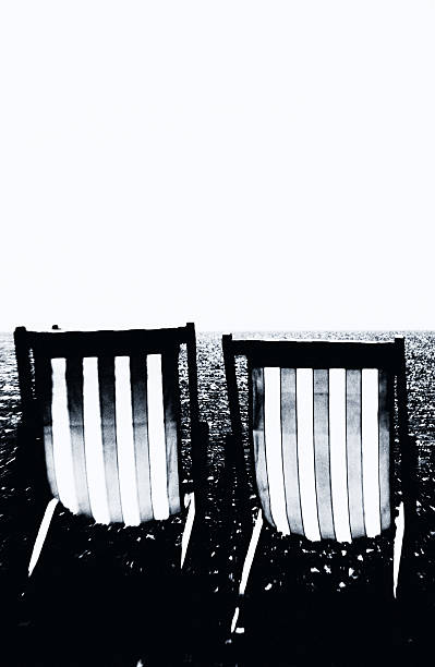 Two empty deck chairs face the shimmering sea, where leisure lingers in absence and the promise of summer feels distant, suspended in light and silence.