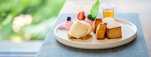 Delicious gourmet honey toast with vanilla ice cream, fresh strawberries, and syrup on a white plate with green garden bokeh. Ideal for cafe dessert menu, food styling, and luxury lifestyle.