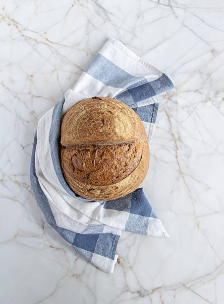 Artisan bread loaf sliced open with checkered napkin on marble surface