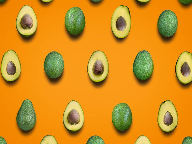 Fresh whole and halved avocados arranged in pattern on orange background overhead view
