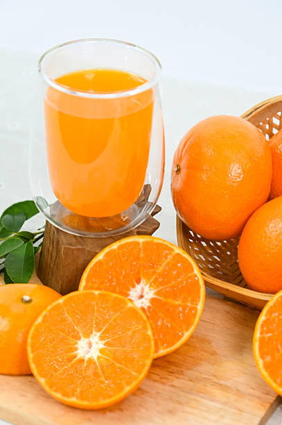 A glass of freshly squeezed orange juice, orange slices with whole oranges, and orange leaves in an organic basket on a white background.