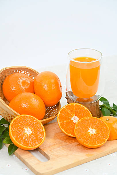 A glass of freshly squeezed orange juice, orange slices with whole oranges, and orange leaves in an organic basket on a white background.