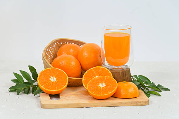 A glass of freshly squeezed orange juice, orange slices with whole oranges, and orange leaves in an organic basket on a white background.