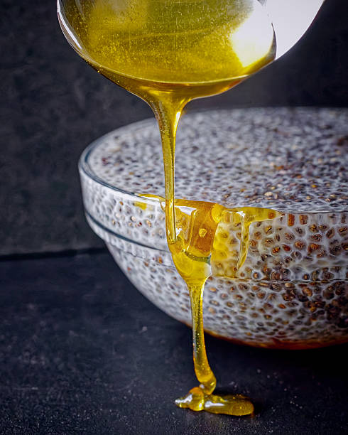 Honey pouring onto chia pudding portrait — dark background amber thread