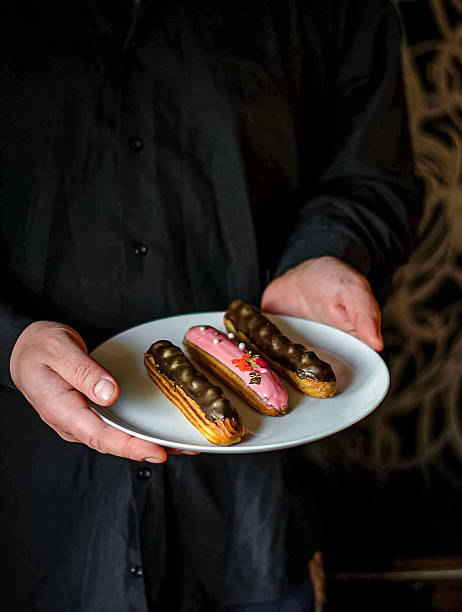 Male hands in a black shirt holding a plate of eclairs.