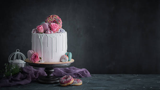 The centerpiece is a meticulously decorated, single-tier light pink cake with elegant white drip icing, sitting gracefully on a sturdy, dark brown wooden cake stand