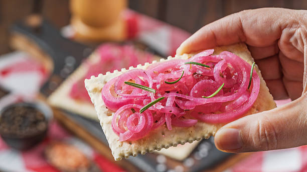 Hand holding cracker with pickled red onions and rosemary