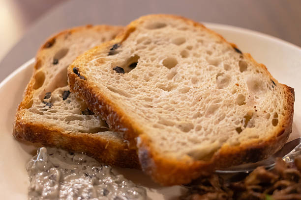 Crusty artisan olive bread slice with creamy herb spread on plate, cozy warm breakfast or snack scene with rustic texture and soft crumb