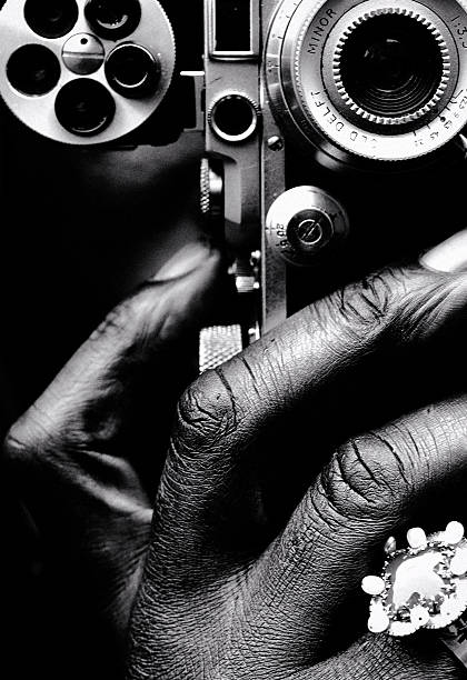 A tactile black-and-white close-up where hand, metal, and memory converge—capturing the intimate mechanics of vision and the quiet authority of the image-maker.