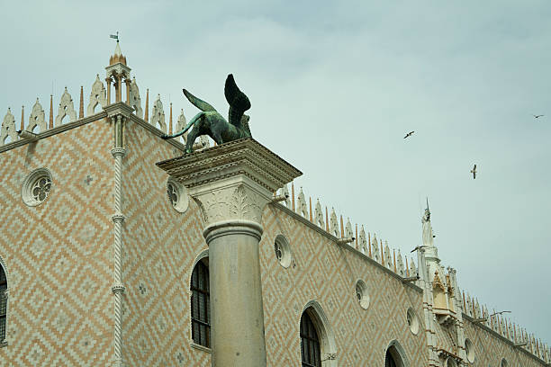 Doge's palace showing intricate architecture, textured facade, and a winged lion statue with birds flying in the background