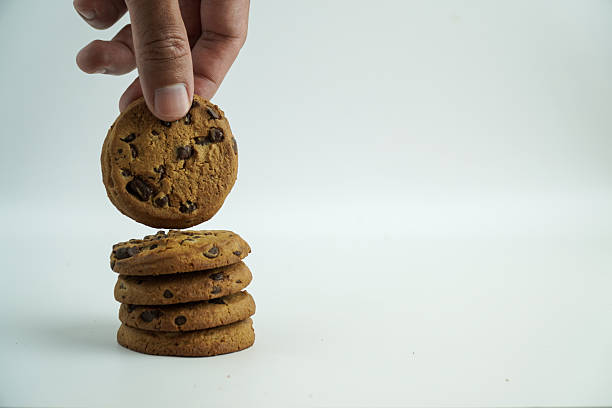 Hand Picking Up a Freshly Baked Chocolate Chip Cookie from a Stack on White