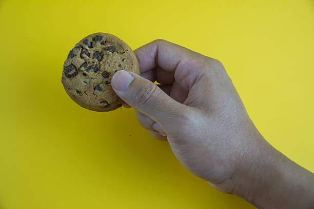 Hand Holding a Delicious Chocolate Chip Cookie Against a Vibrant Yellow Background
