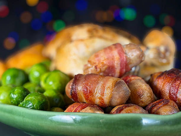 Close-up image Sunday roast / Christmas dinner, all the trimmings on green serving dish, whole roast chicken, surrounded by side dishes of Brussel sprouts, roast potatoes, pigs in blankets, illuminated multicoloured fairy light background