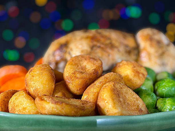 Close-up image of Sunday roast / Christmas dinner with all the trimmings on green serving dish, whole roast chicken, surrounded by side dishes of Brussel sprouts, roast potatoes, sliced carrots, illuminated multicoloured fairy light background