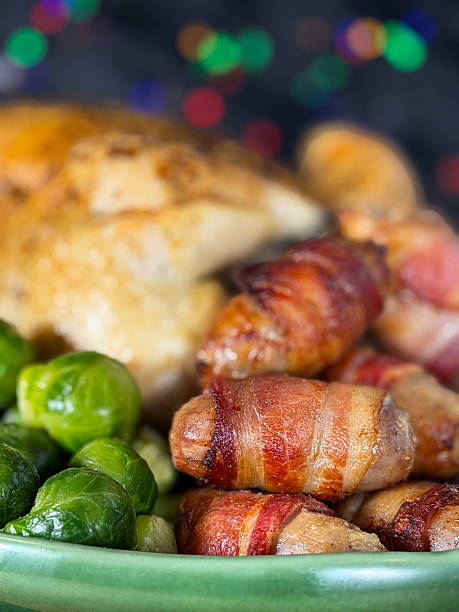 Full frame image Sunday roast / Christmas dinner, all the trimmings on green serving dish, whole roast chicken, surrounded by side dishes of Brussel sprouts, pigs in blankets, illuminated multicoloured fairy light background