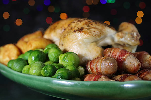 Close-up image Sunday roast / Christmas dinner, all the trimmings on green serving dish, whole roast chicken, surrounded by side dishes of Brussel sprouts, roast potatoes, pigs in blankets, illuminated multicoloured fairy light background