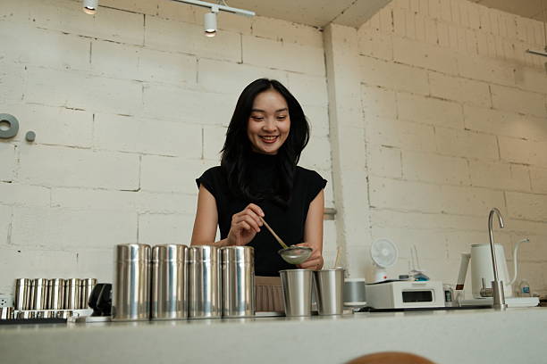 Young adult woman smiling, preparing a matcha beverage by sifting green tea powder in a modern cafe kitchen