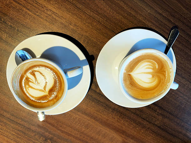 Two cups of fresh cappuccino with heart shape latte art on a dark wooden table