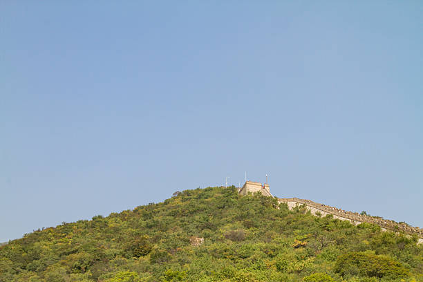 Iconic Great Wall of China structure with a watchtower, running along a lush green mountain ridge under a clear blue sky, representing history, triumph, and ancient architecture