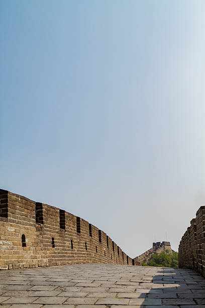 Ancient stone bricks and walls of the Great Wall of China winding across a sunny landscape, showing a watchtower in the distance against a clear blue sky