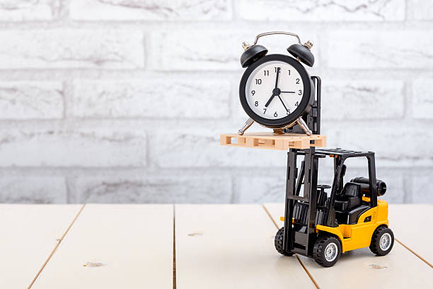 A forklift lifts a black vintage alarm clock on a wooden table with copy space for text. Selective focus.