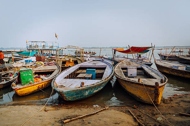 Wooden boats docked along the Ganges riverbank in Varanasi, India, showing colorful canopies, worn textures and local life at the ghats; a vibrant travel and cultural scene by the water.
