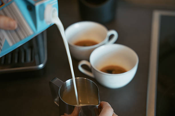 Pouring Milk into Stainless Steel Pitcher with Espresso Cups in Background
