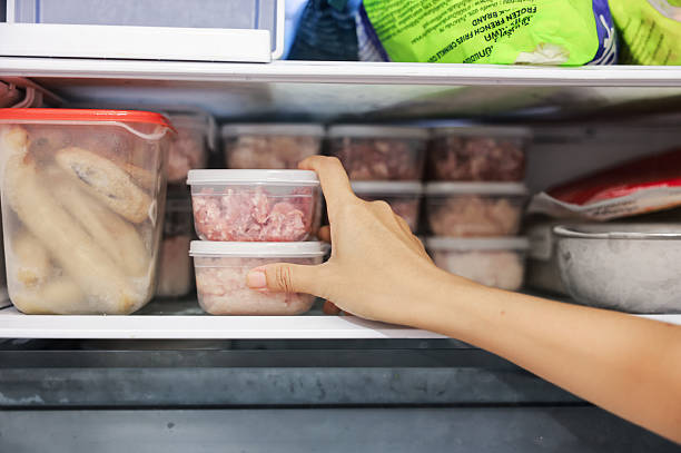 Close up of woman hand taking clear plastic food containers with raw minced meat from the freezer. Organizing refrigerator, daily food preparation, meal prep, household routine and kitchen storage.