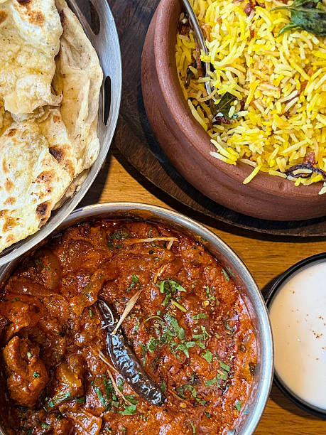 Image of overhead view of aromatic biryani rice, parathas, naan bread, served alongside kadhai chicken tikka masala, butter chicken curry, Indian meal