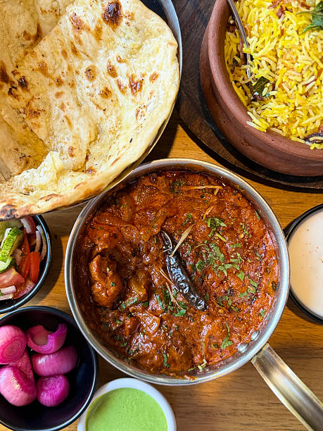 Image of overhead view of fragrant biryani rice with soft parathas, naan bread, served alongside kadhai chicken tikka masala, buttery chicken curry, authentic Indian meal