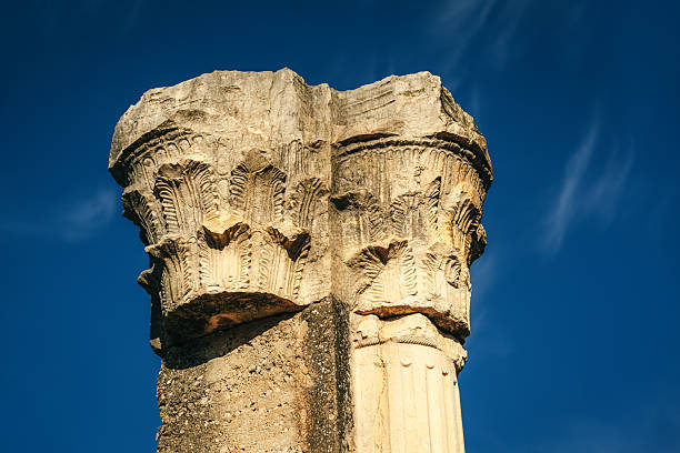 Sunlit carved Corinthian column at the archaeological site of Volubilis, Morocco, highlighting ancient Roman architecture, texture and heritage at a UNESCO World Heritage ruin under a clear blue sky.