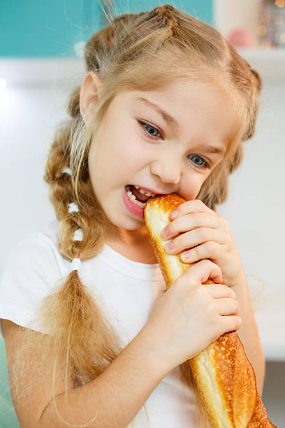 Portrait of a little blonde girl biting a fresh baguette