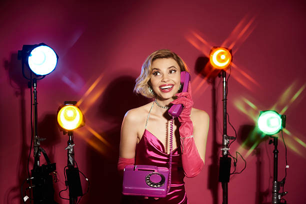 A stylish blonde woman joyfully interacts with a vintage phone inside a lively studio.