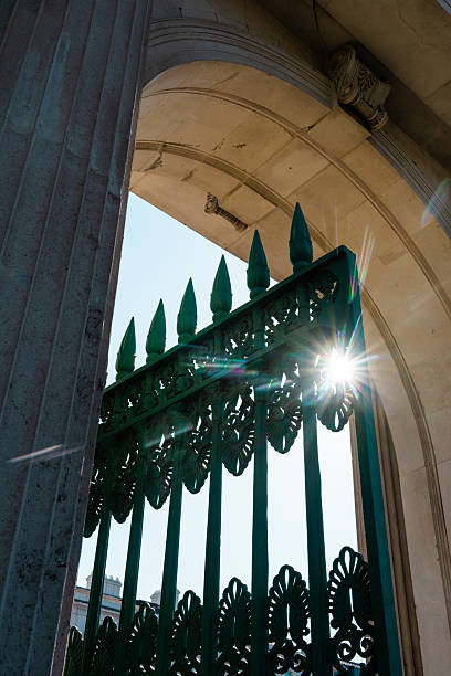 Ornate green wrought iron gate with sun starburst through architectural stone archway